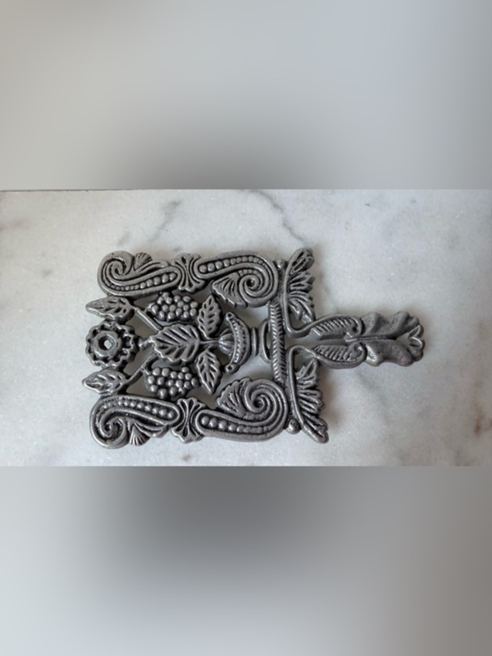 vintage silver-toned metal trivet featuring a decorative design grapes scrolls.